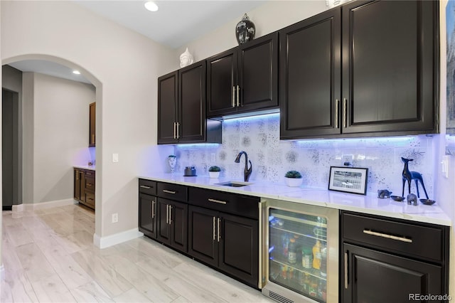8000 Raphael Ln, Littleton, CO 80125 - kitchen featuring wine cooler, dark cabinets, arched walkways, light countertops, and backsplash