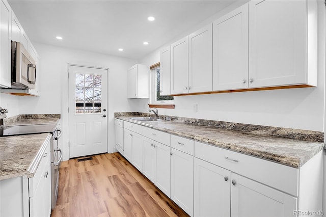 kitchen with light wood finished floors, appliances with stainless steel finishes, white cabinetry, a sink, and recessed lighting