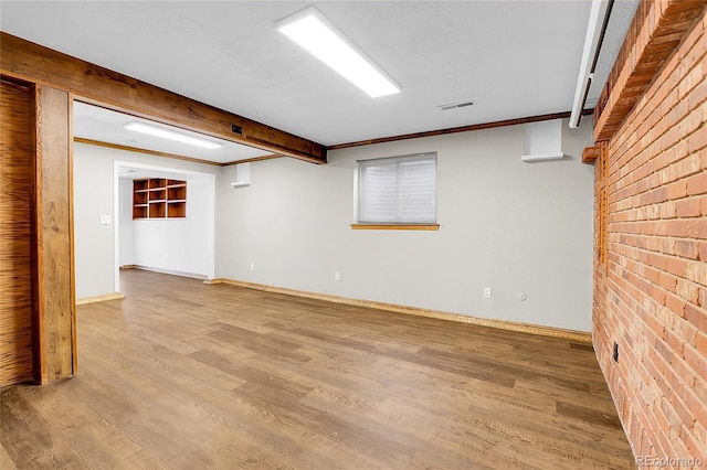 spare room featuring baseboards, visible vents, brick wall, and wood finished floors