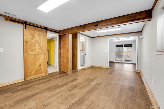 spare room featuring beam ceiling, visible vents, a barn door, wood finished floors, and baseboards