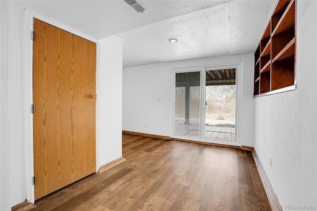 spare room with a textured ceiling, wood finished floors, visible vents, and baseboards