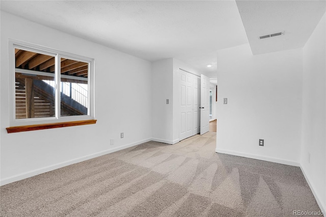 spare room featuring light carpet, baseboards, visible vents, and a textured ceiling