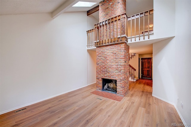 2713 W Long Dr Unit C, Littleton, CO 80120 - unfurnished living room featuring wood finished floors, beamed ceiling, stairs, high vaulted ceiling, and a brick fireplace