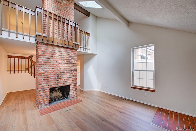 2713 W Long Dr Unit C, Littleton, CO 80120 - unfurnished living room featuring a skylight, beamed ceiling, wood finished floors, a brick fireplace, and high vaulted ceiling
