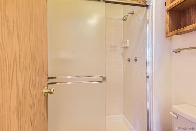 bathroom featuring a shower with door and toilet