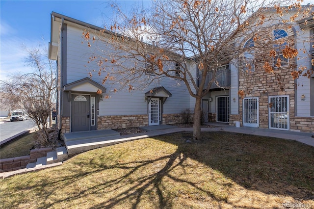 view of front of home with stone siding, a balcony, and a front yard