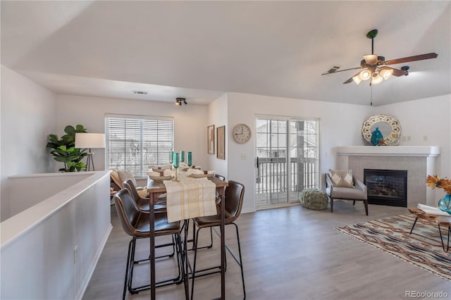 dining area with a glass covered fireplace, a ceiling fan, visible vents, and wood finished floors