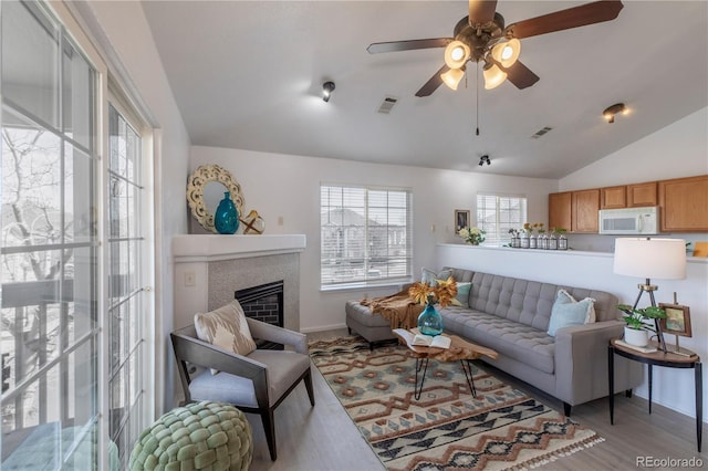 living area with lofted ceiling, wood finished floors, visible vents, and a tile fireplace