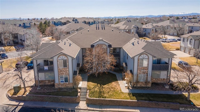 view of front facade featuring a residential view, stone siding, and roof with shingles