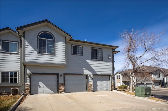 multi unit property featuring stone siding, an attached garage, concrete driveway, and central AC