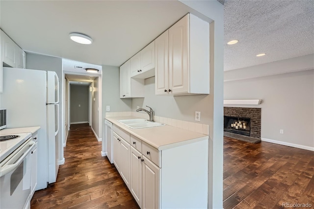 kitchen featuring a fireplace, white cabinets, sink, white appliances, and dark hardwood / wood-style flooring