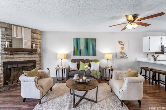 living room featuring a fireplace, a textured ceiling, a ceiling fan, and wood finished floors