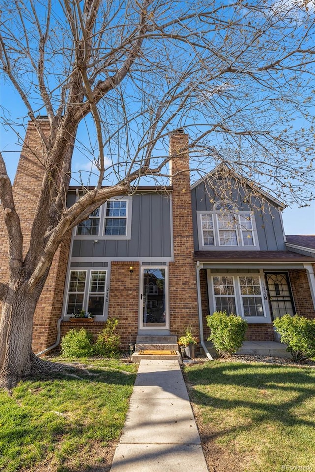 traditional-style house with a front yard, a chimney, brick siding, and board and batten siding