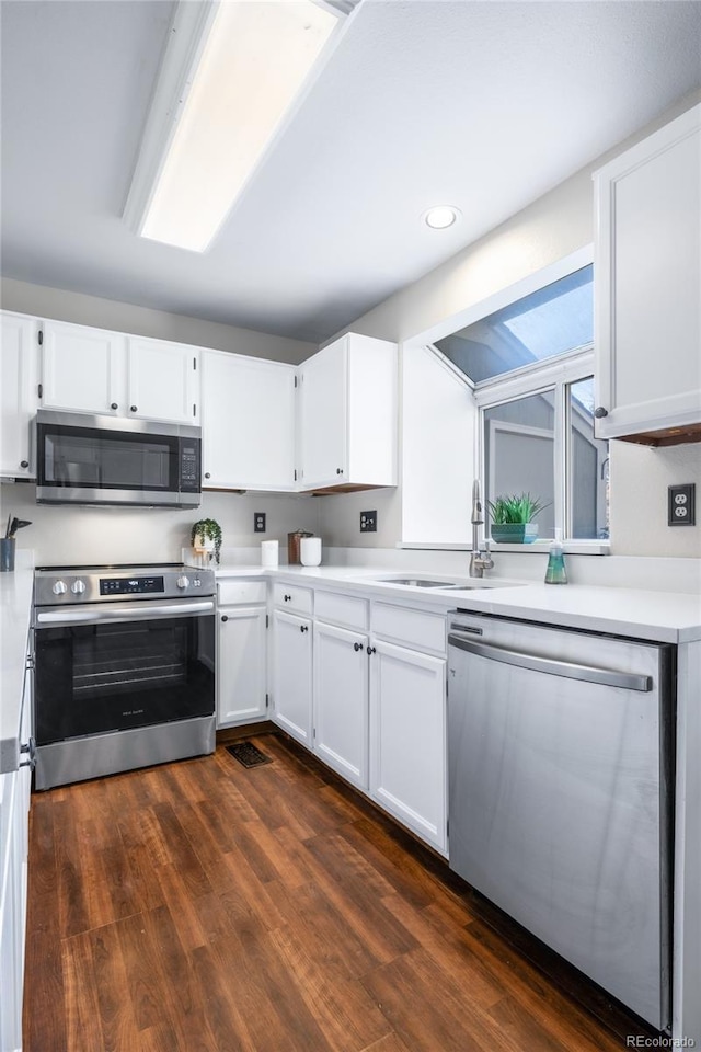 kitchen featuring stainless steel appliances, a sink, white cabinetry, light countertops, and dark wood-style floors