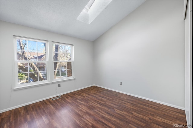 spare room with a textured ceiling, wood finished floors, baseboards, and vaulted ceiling with skylight