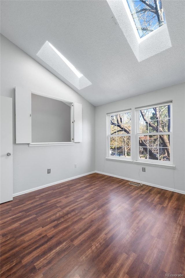 spare room with a textured ceiling, baseboards, vaulted ceiling with skylight, and wood finished floors