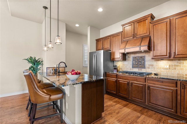 kitchen featuring black gas stovetop, tasteful backsplash, dark stone counters, freestanding refrigerator, and custom exhaust hood