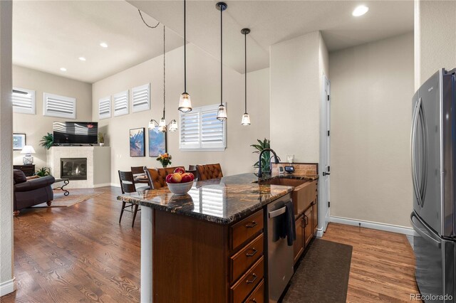 kitchen featuring stainless steel appliances, a glass covered fireplace, dark stone countertops, and wood finished floors