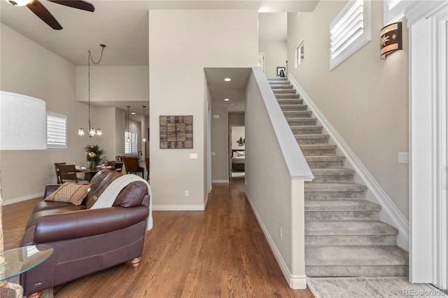interior space featuring baseboards, stairs, wood finished floors, and ceiling fan with notable chandelier