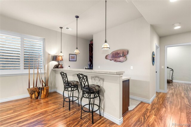 kitchen featuring light countertops, a breakfast bar, hanging light fixtures, visible vents, and wood finished floors