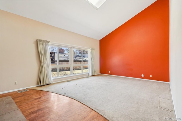 spare room featuring high vaulted ceiling, visible vents, baseboards, and wood finished floors