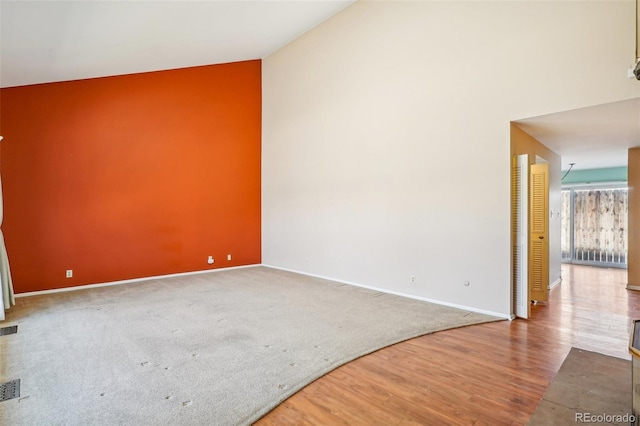 spare room featuring carpet floors, visible vents, a high ceiling, wood finished floors, and baseboards