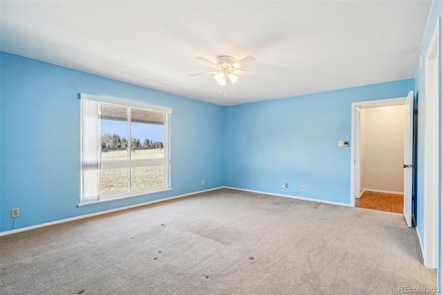 carpeted spare room with a ceiling fan and baseboards