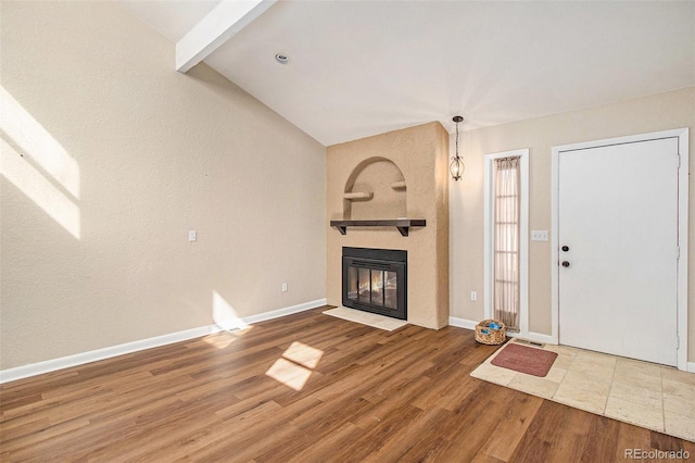 unfurnished living room featuring vaulted ceiling with beams, wood finished floors, baseboards, and a large fireplace