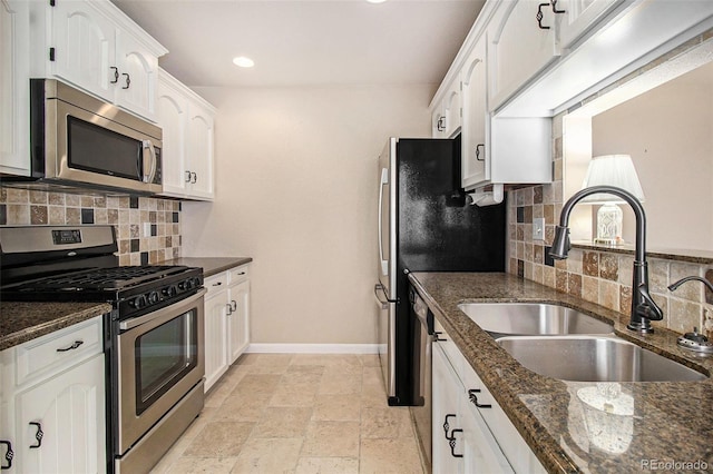 kitchen featuring a sink, dark stone countertops, stone tile floors, appliances with stainless steel finishes, and baseboards