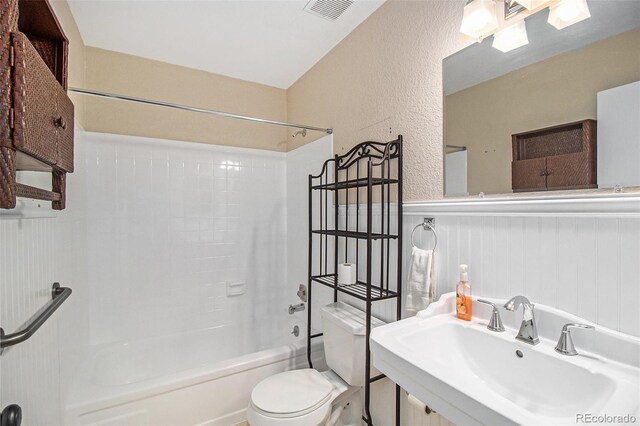 bathroom with visible vents, shower / washtub combination, toilet, wainscoting, and a sink