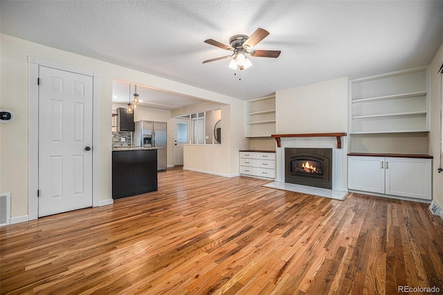 unfurnished living room with ceiling fan, light hardwood / wood-style floors, and a textured ceiling