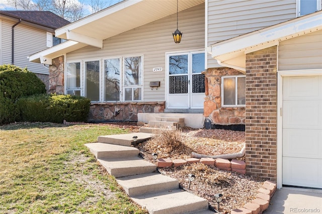 entrance to property with an attached garage, a lawn, brick siding, and stone siding