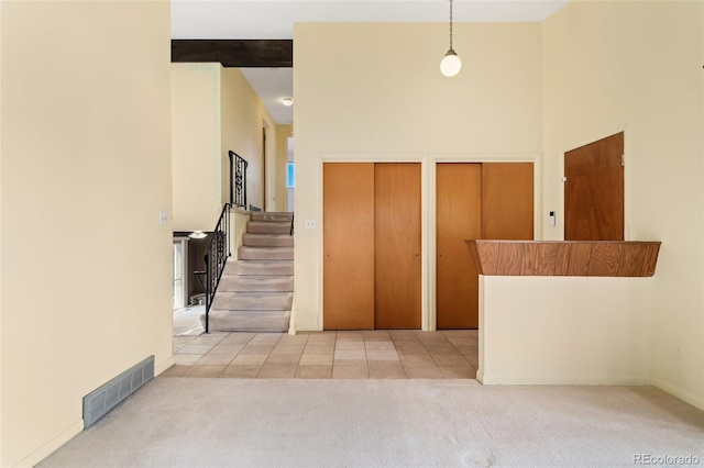 carpeted foyer with tile patterned flooring, visible vents, beamed ceiling, stairway, and a towering ceiling