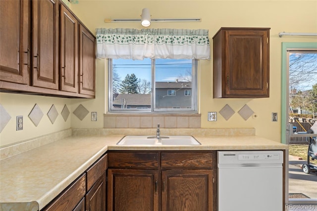 kitchen featuring light countertops, dark brown cabinets, white dishwasher, and a sink