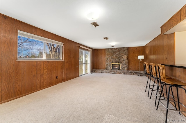 interior space featuring visible vents, carpet, a stone fireplace, and wooden walls