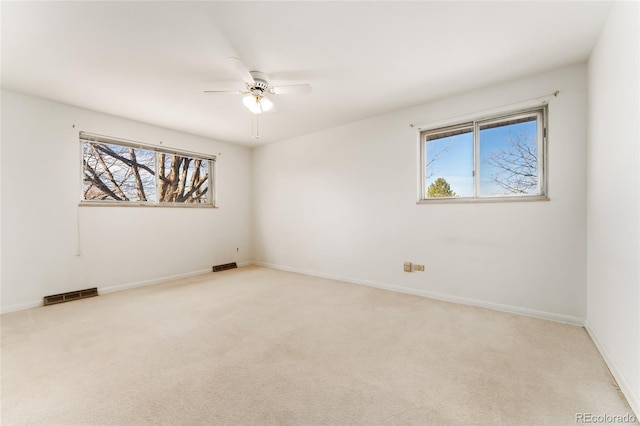 empty room featuring visible vents, light colored carpet, baseboards, and a ceiling fan