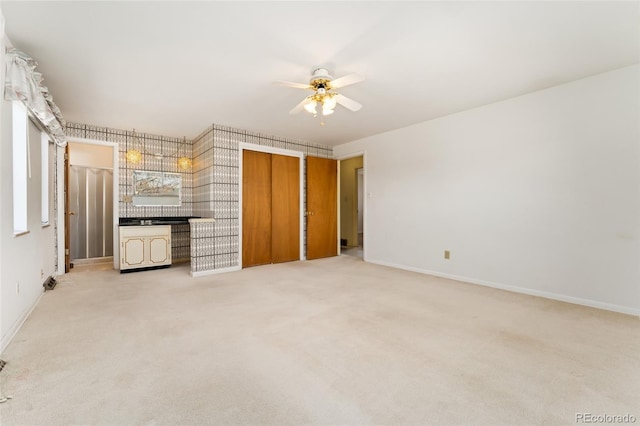 unfurnished living room featuring ceiling fan, baseboards, and light carpet