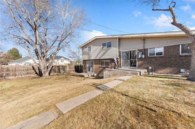 back of house featuring brick siding, a lawn, and fence