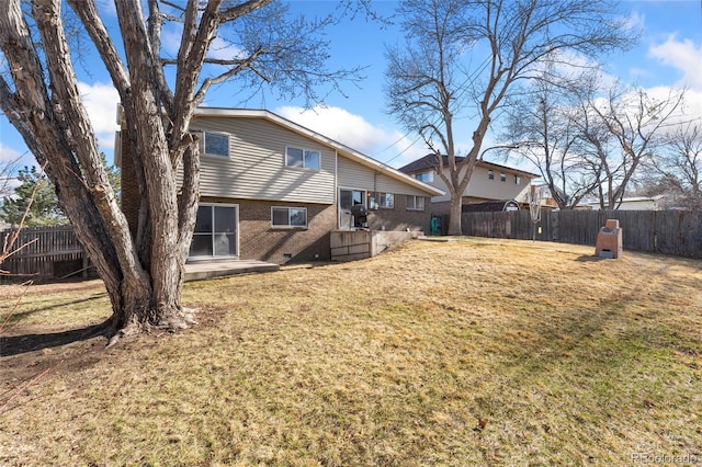 rear view of house with crawl space, a fenced backyard, brick siding, and a lawn