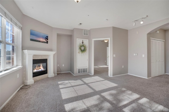 unfurnished living room with a wealth of natural light, a tile fireplace, visible vents, and carpet flooring