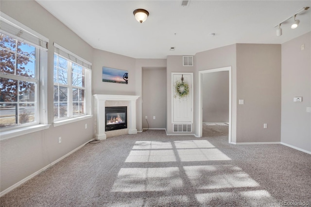 unfurnished living room with baseboards, visible vents, carpet flooring, and a glass covered fireplace