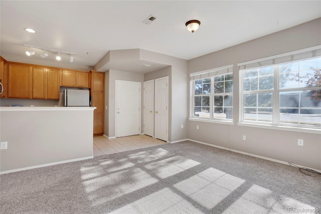 kitchen featuring light tile patterned floors, light colored carpet, visible vents, baseboards, and freestanding refrigerator