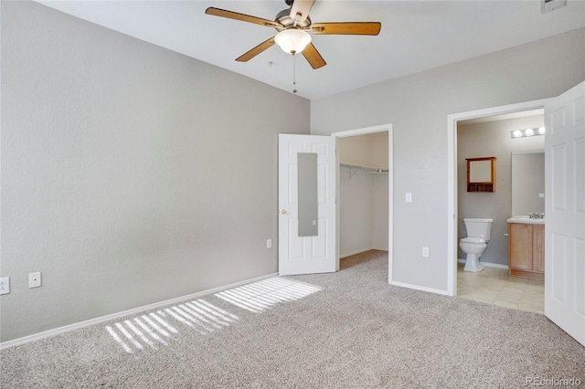 unfurnished bedroom with light carpet, baseboards, ensuite bath, a walk in closet, and a closet