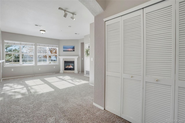 unfurnished living room with baseboards, visible vents, a glass covered fireplace, carpet flooring, and track lighting