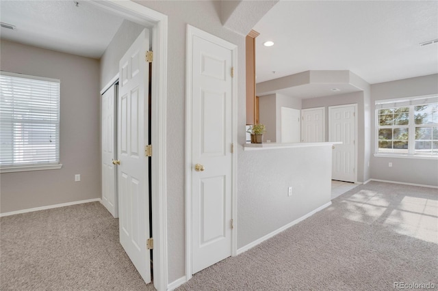 corridor featuring baseboards, a wealth of natural light, and light colored carpet