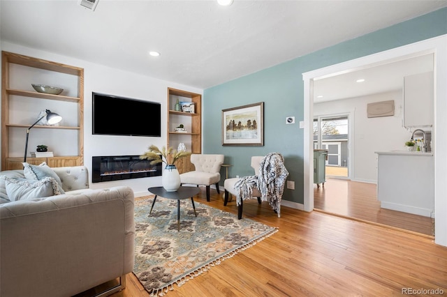 living room featuring sink, light wood-type flooring, and built in features