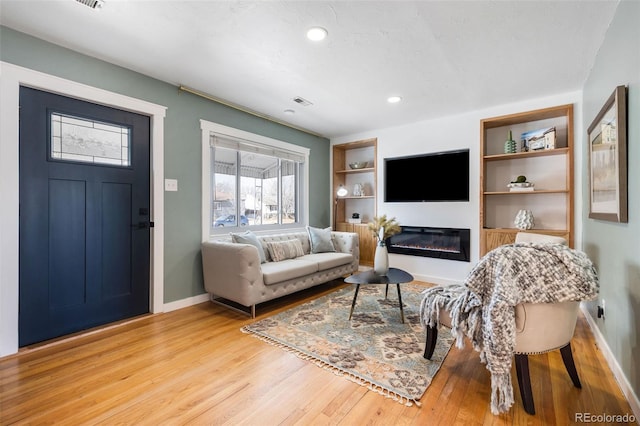 living room with built in shelves and light hardwood / wood-style flooring