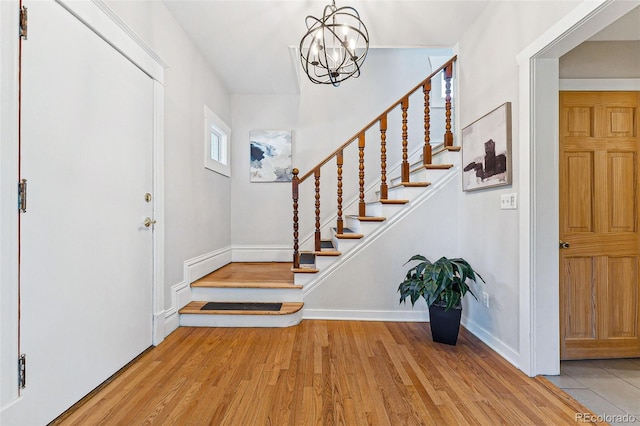 foyer entrance featuring stairs, a chandelier, baseboards, and wood finished floors