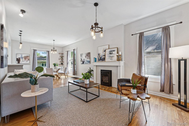 living room with hardwood / wood-style flooring, a tiled fireplace, baseboards, and a notable chandelier