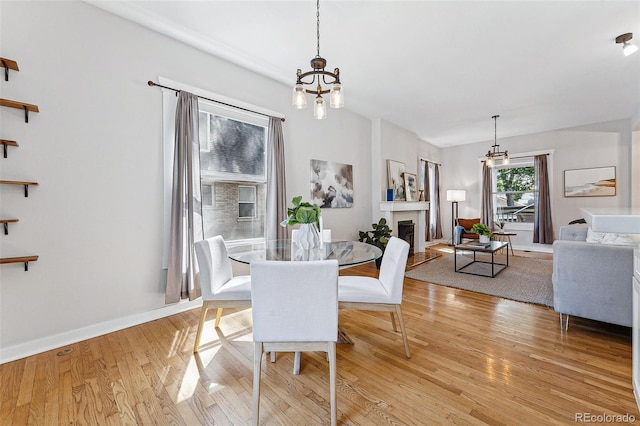 dining room with a notable chandelier, light wood-type flooring, a fireplace, and baseboards